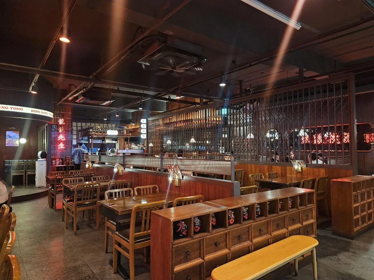A dimly lit restaurant interior styled with retro Hong Kong aesthetics, featuring dark wooden tables and chairs, iron-gr