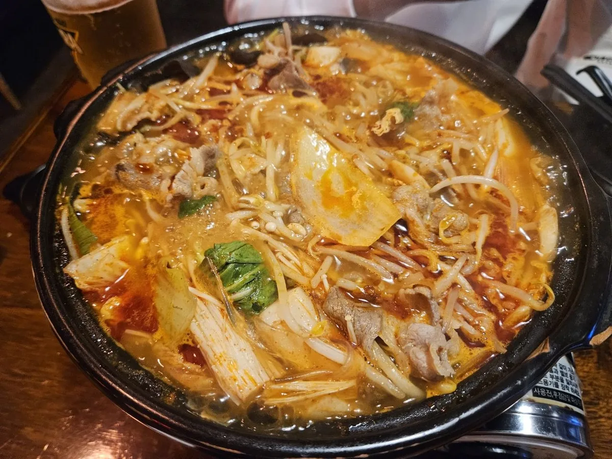 A large black iron pot filled with Hwasan mala jeongol (volcanic spicy hot pot) after cooking, featuring a rich orange-r