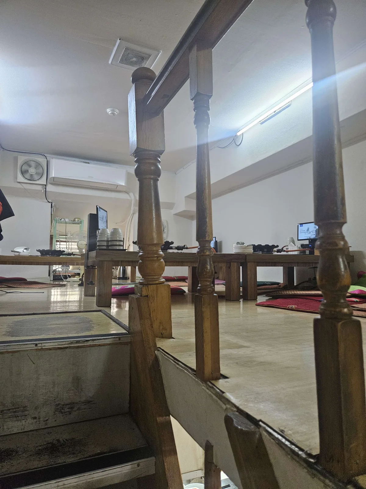 The second floor dining area of a Korean restaurant features low wooden tables with floor cushions for seated dining, vi