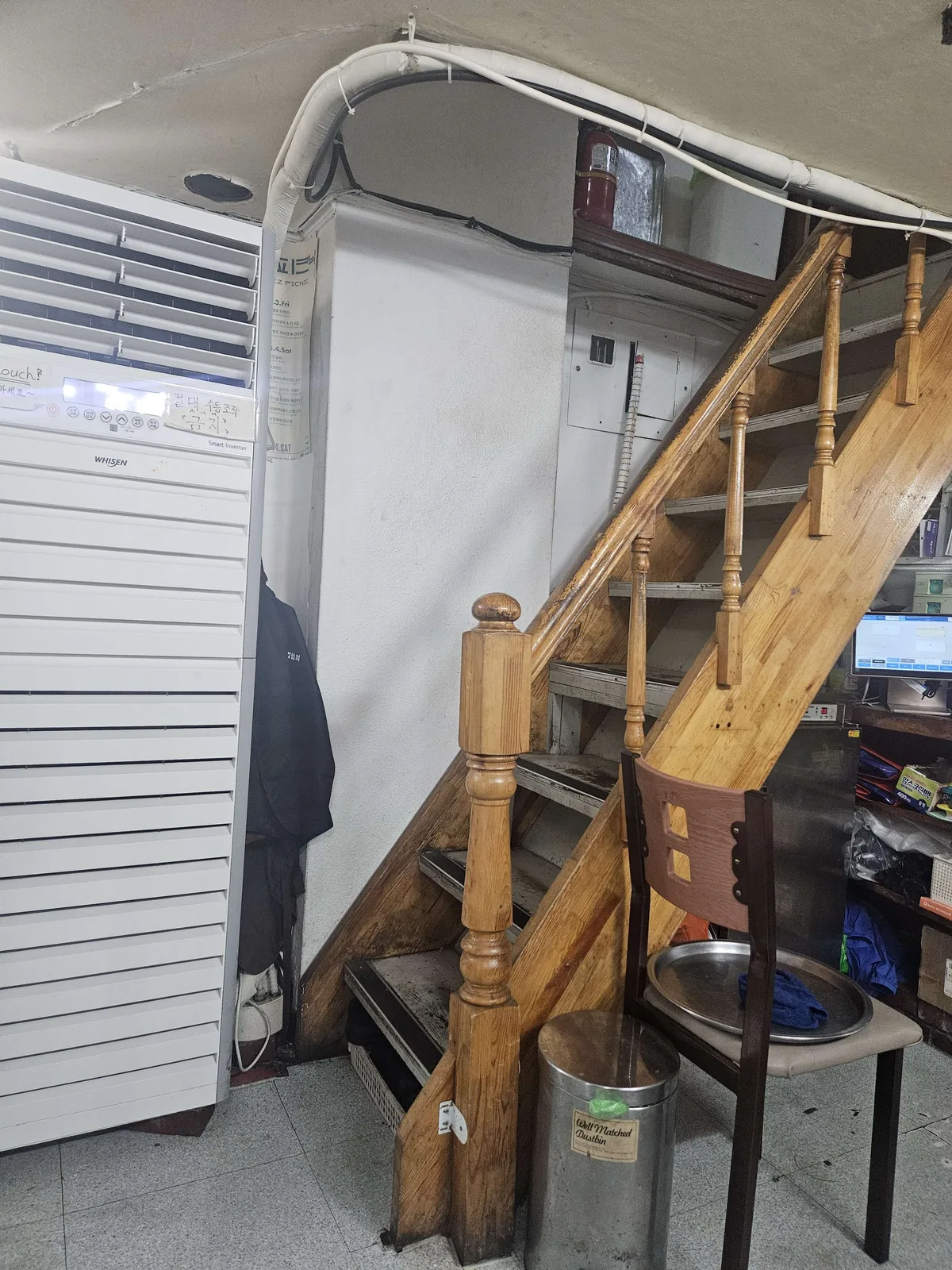 A narrow wooden staircase with turned balusters leads up to the second floor of a restaurant, flanked by a large floor-s