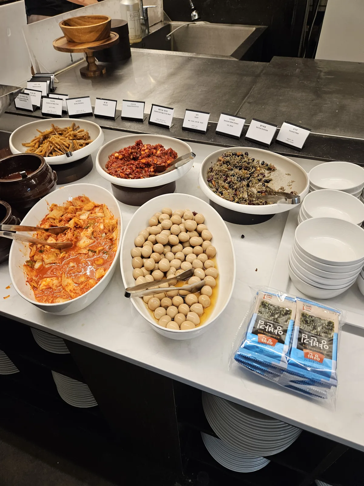 The Korean banchan station — kimchi, braised beans, anchovies, and gim