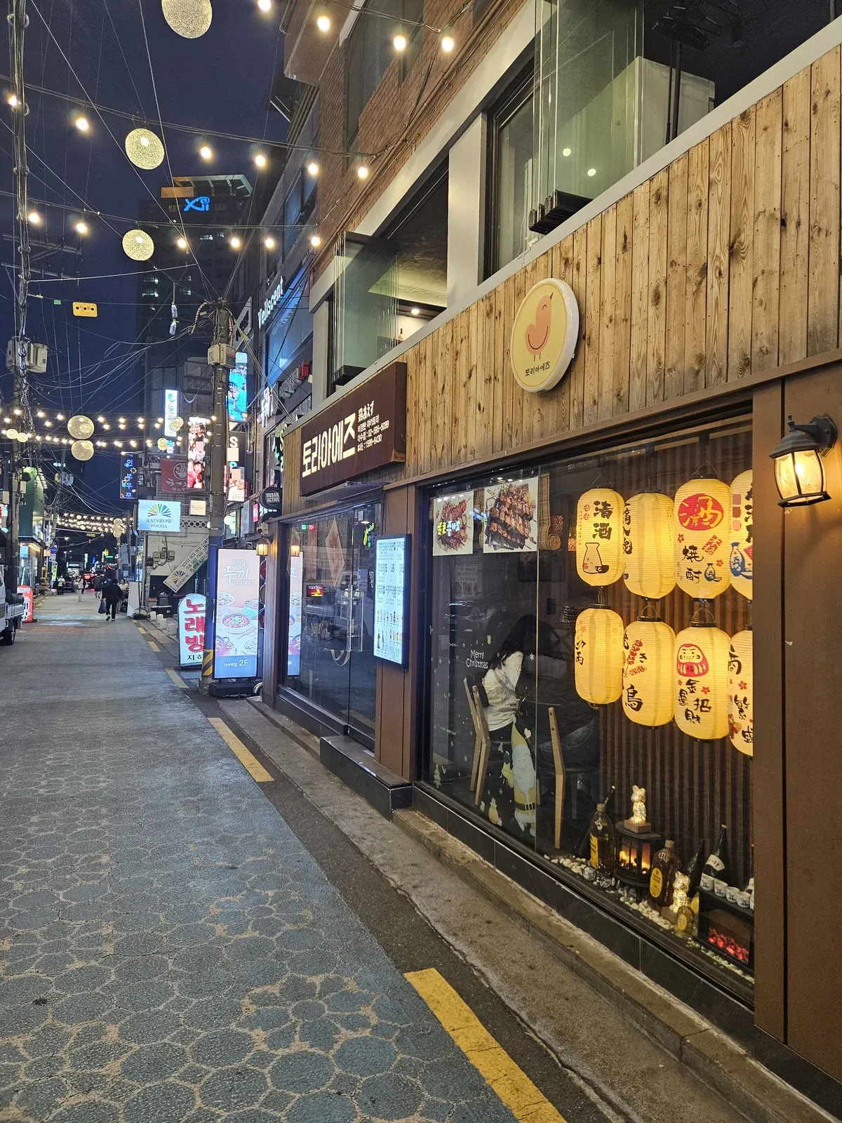 The alley between Isu and Sadang after dark — string lights, neon, and about a dozen places still serving